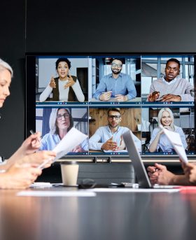 Global corporation online videoconference in meeting room with diverse people sitting in modern office and multicultural multiethnic colleagues on big screen monitor. Business technologies concept.