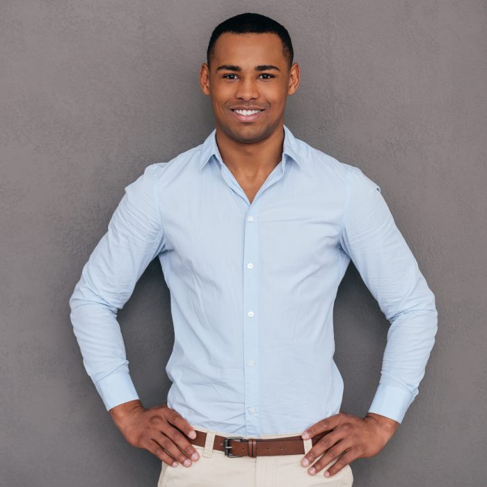 Confident and handsome. Confident young African man keeping arms crossed and looking at camera while standing against grey background