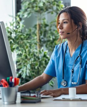 Shot of female doctor talking with earphone while explaining medical treatment to patient through a video call with computer in the consultation.